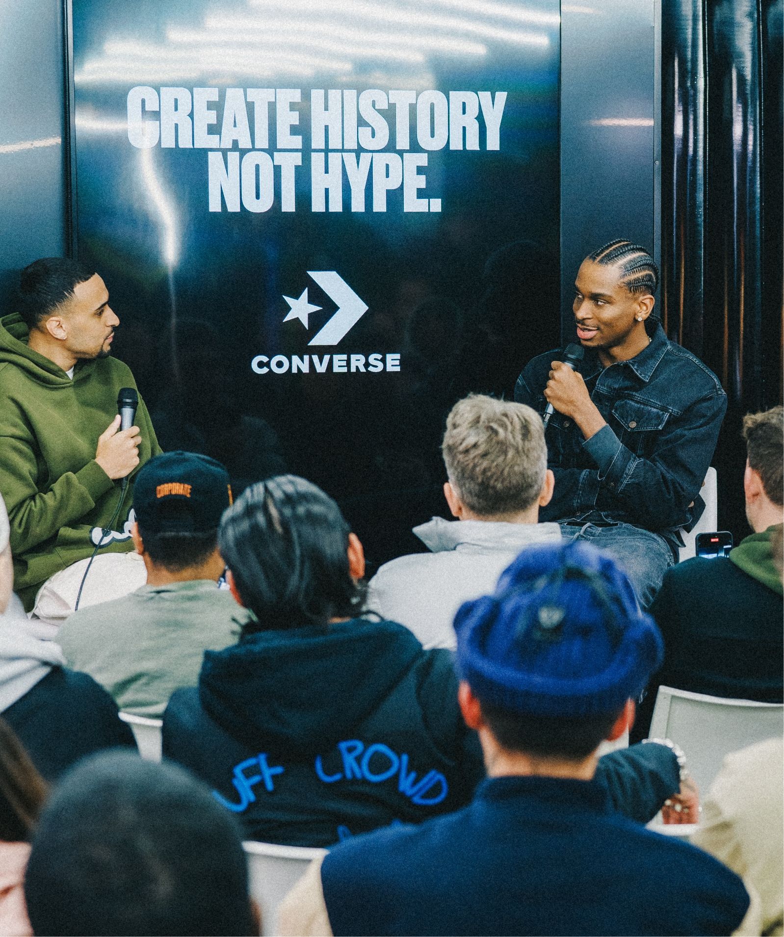 Shai Gilgeous-Alexander talks with moderator and group of seated people. A screen displays the message Create History Not Hype with a Converse logo