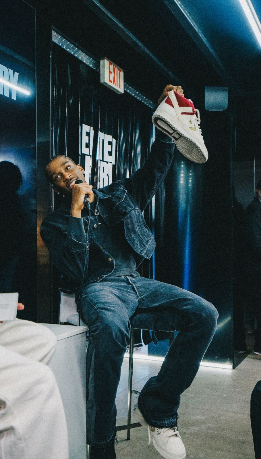 Shai Gilgeous-Alexander sits on stool with microphone and holds up a classic pair of Converse sneakers