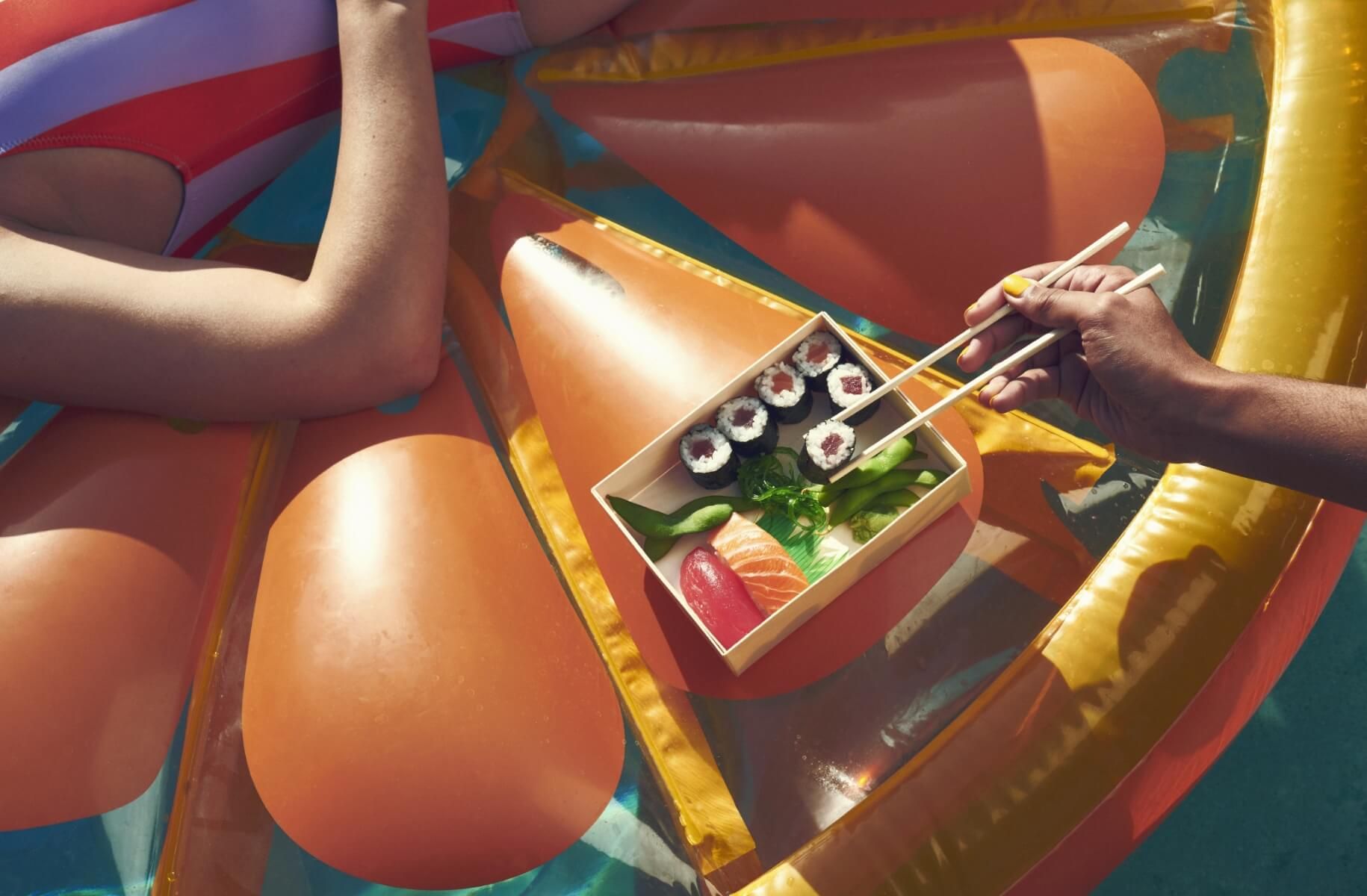 Close up of woman using chopsticks to pick up sushi while on a float in pool