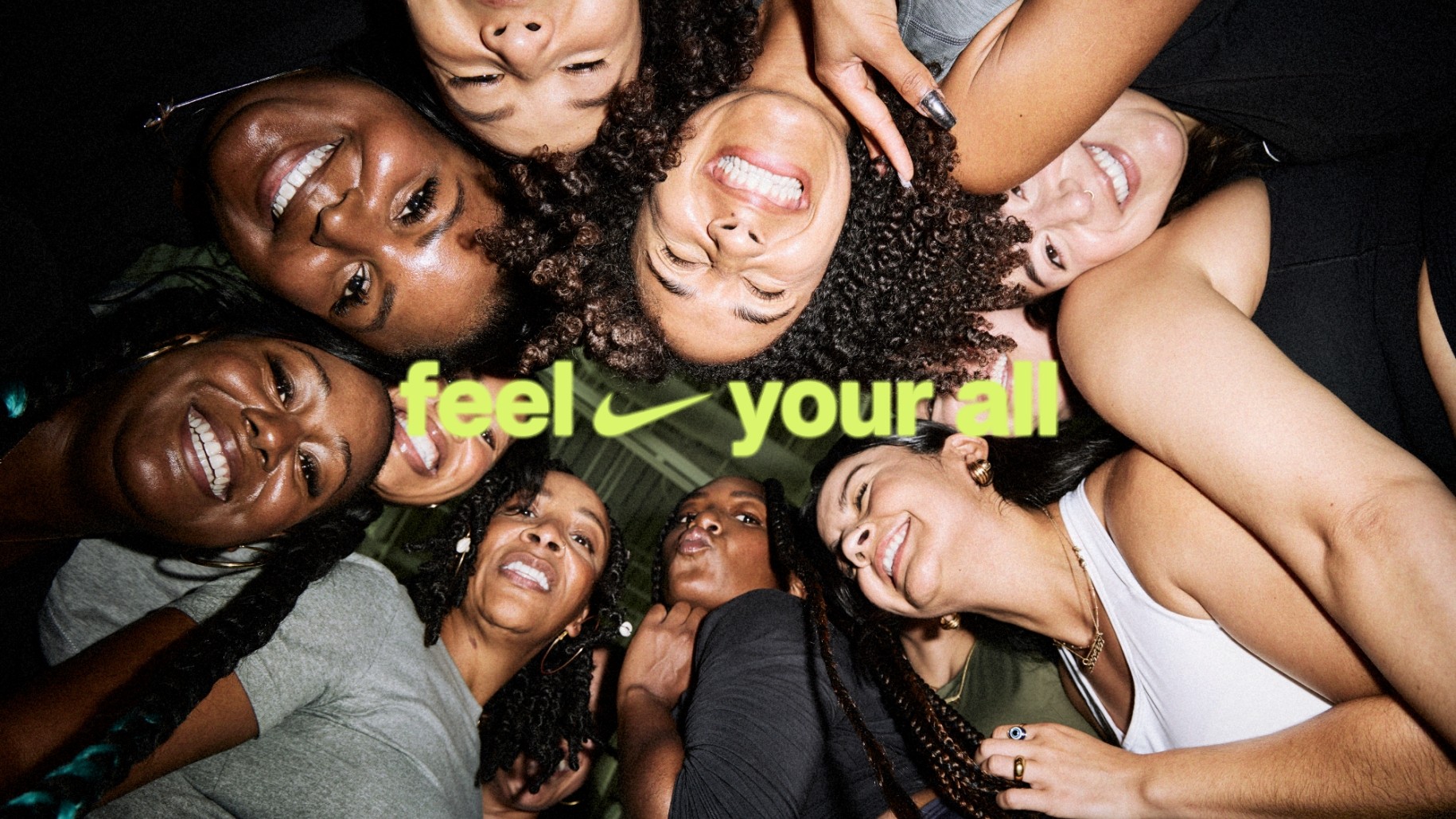 Group of 12 women in circle looking down at camera laughing and posing. feel your all text nike swoosh