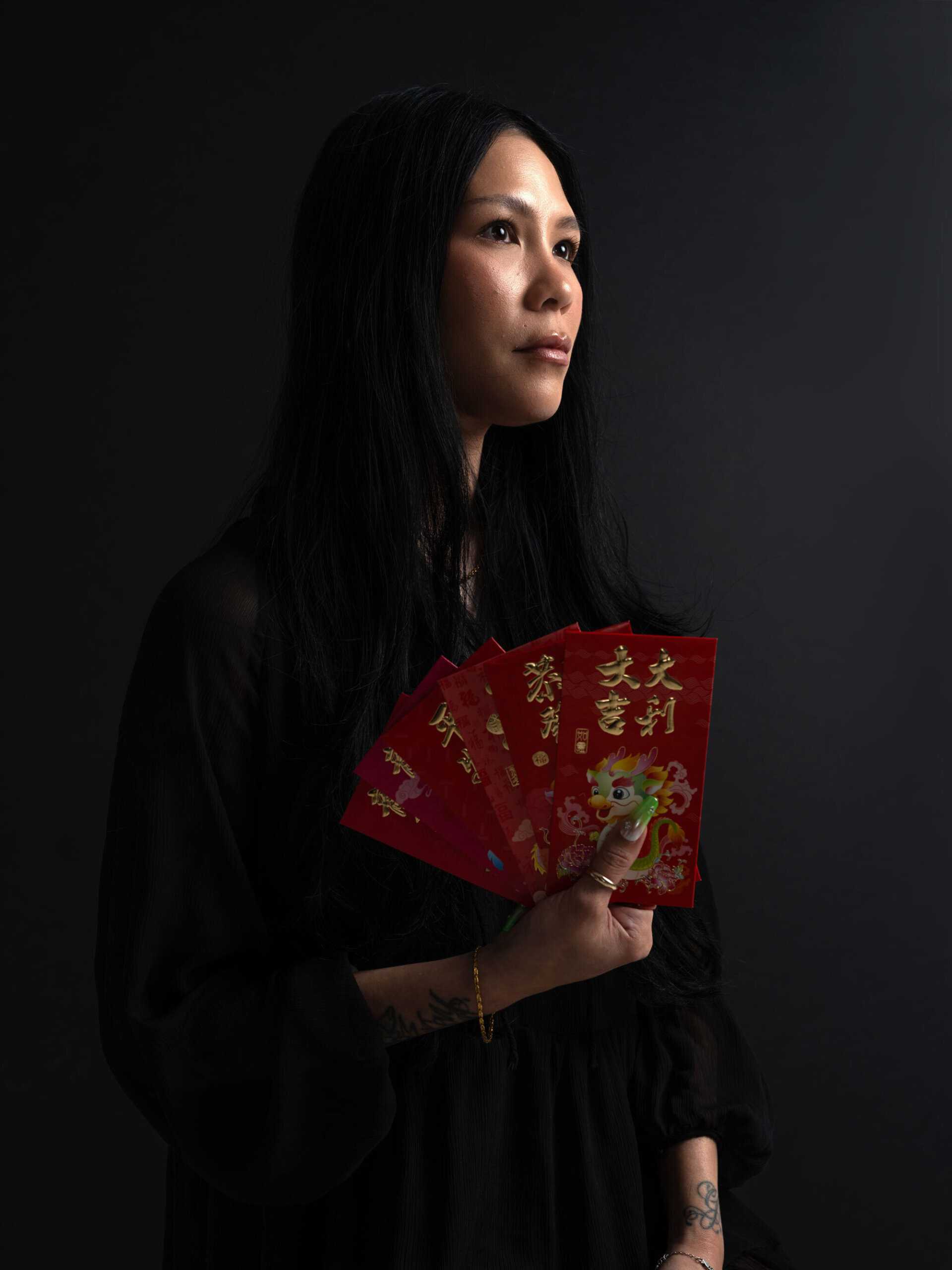 A person with long hair holds several red envelopes with Chinese characters and a dragon design, standing against a dark background.