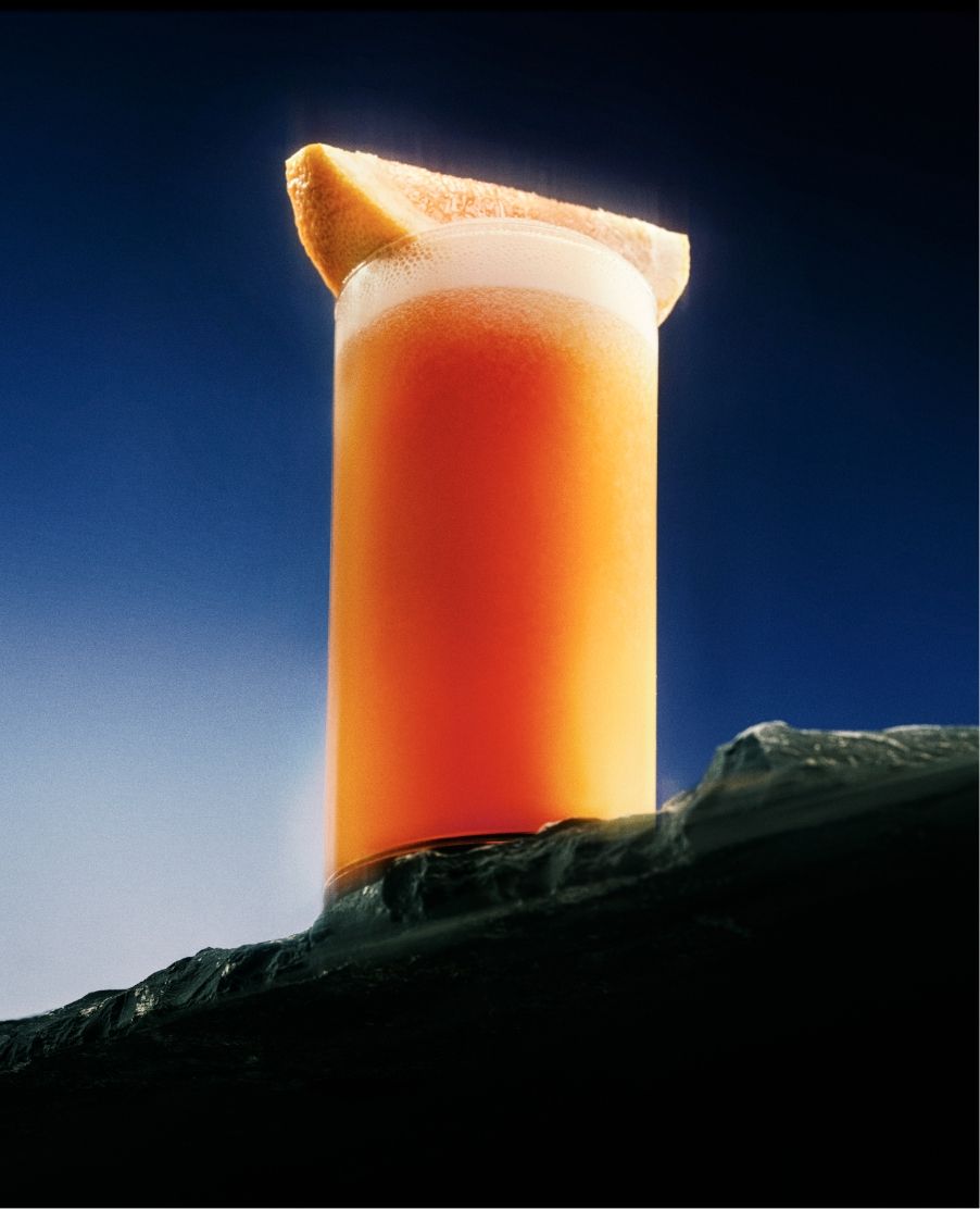 Glass of orange liquid with orange on black rock surface with