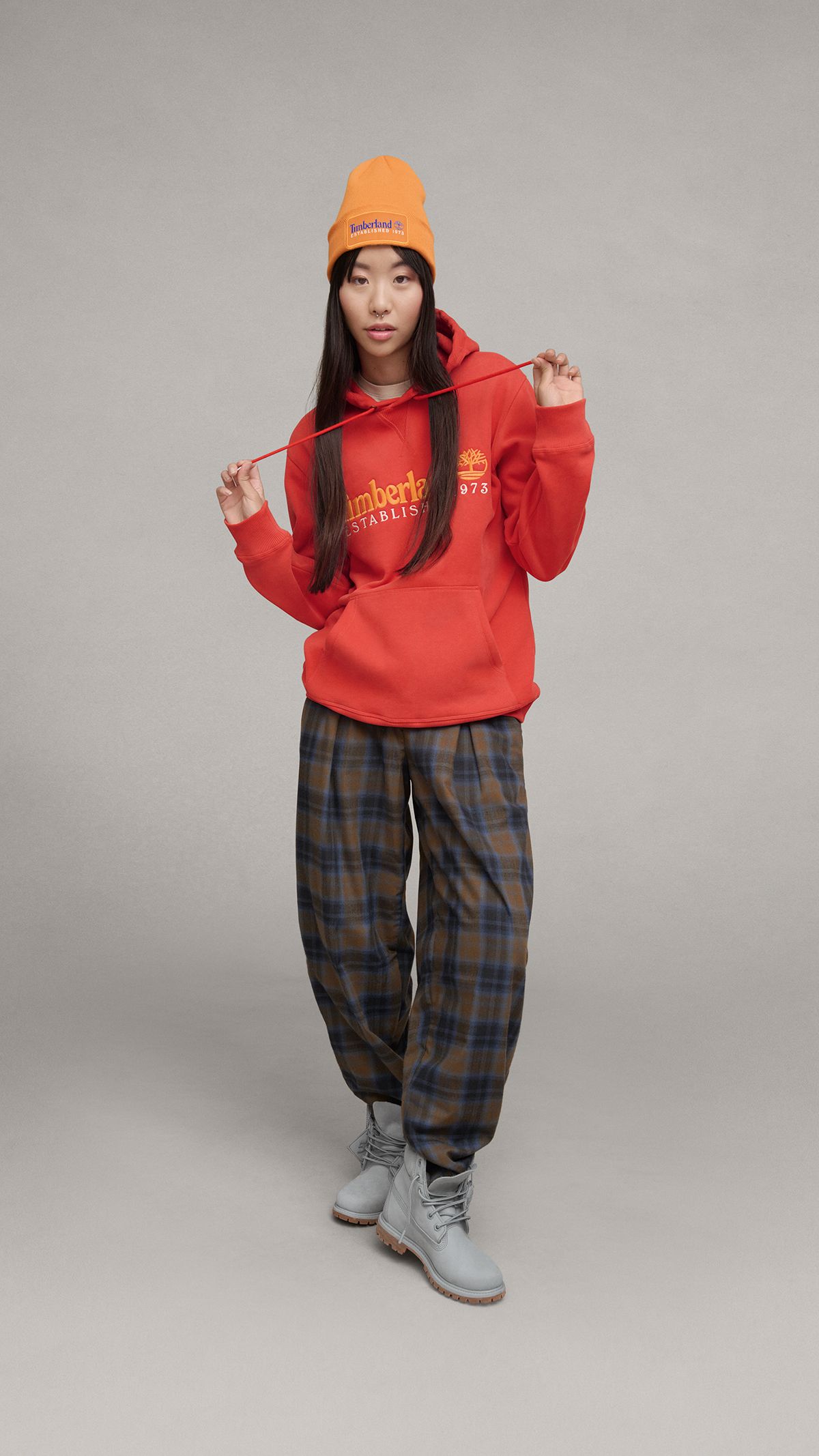 A woman wearing a red hoodie, plaid pants and quarry gray Timberland boots.