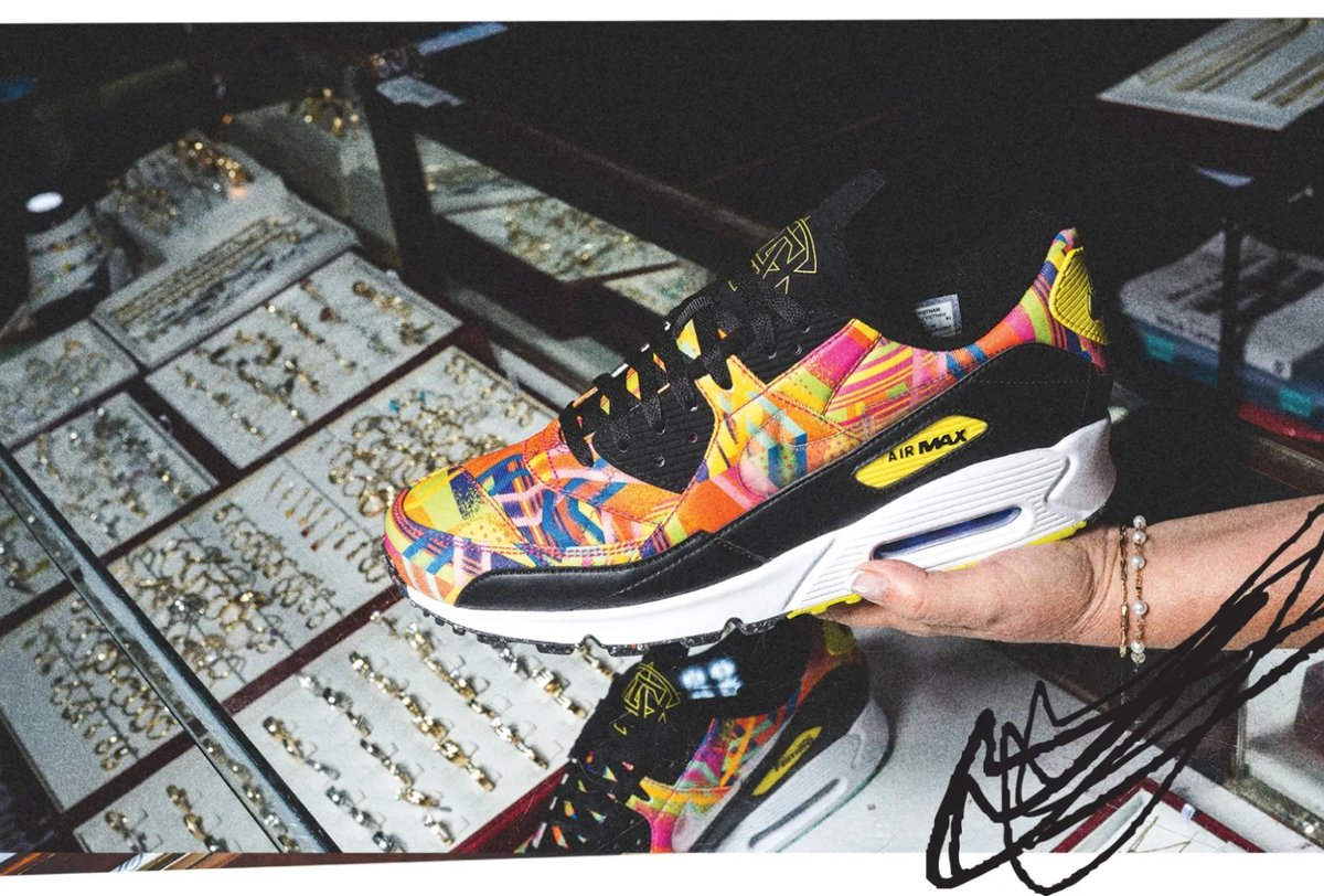 A person holds a colorful Nike Air Max sneaker above a glass display case filled with jewelry.