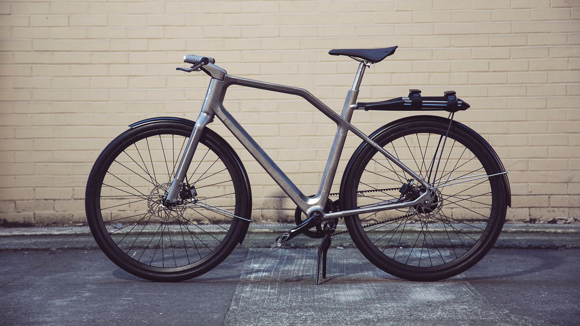 A modern bicycle with a sleek, metallic frame parked against a yellow brick wall.