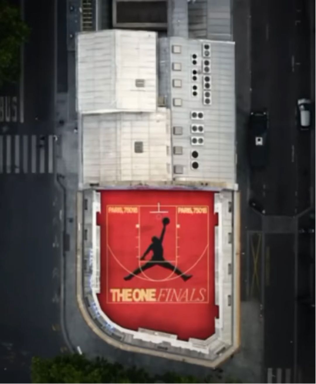 Aerial view of a red basketball court with "THE ONE FINALS" and a large black Michael Jordan silhouette logo, surrounded by city streets and buildings.