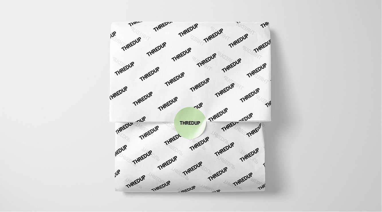 A package wrapped in white tissue paper printed with repeated "THREDUP" logos, sealed with a light green circular sticker also labeled "THREDUP.