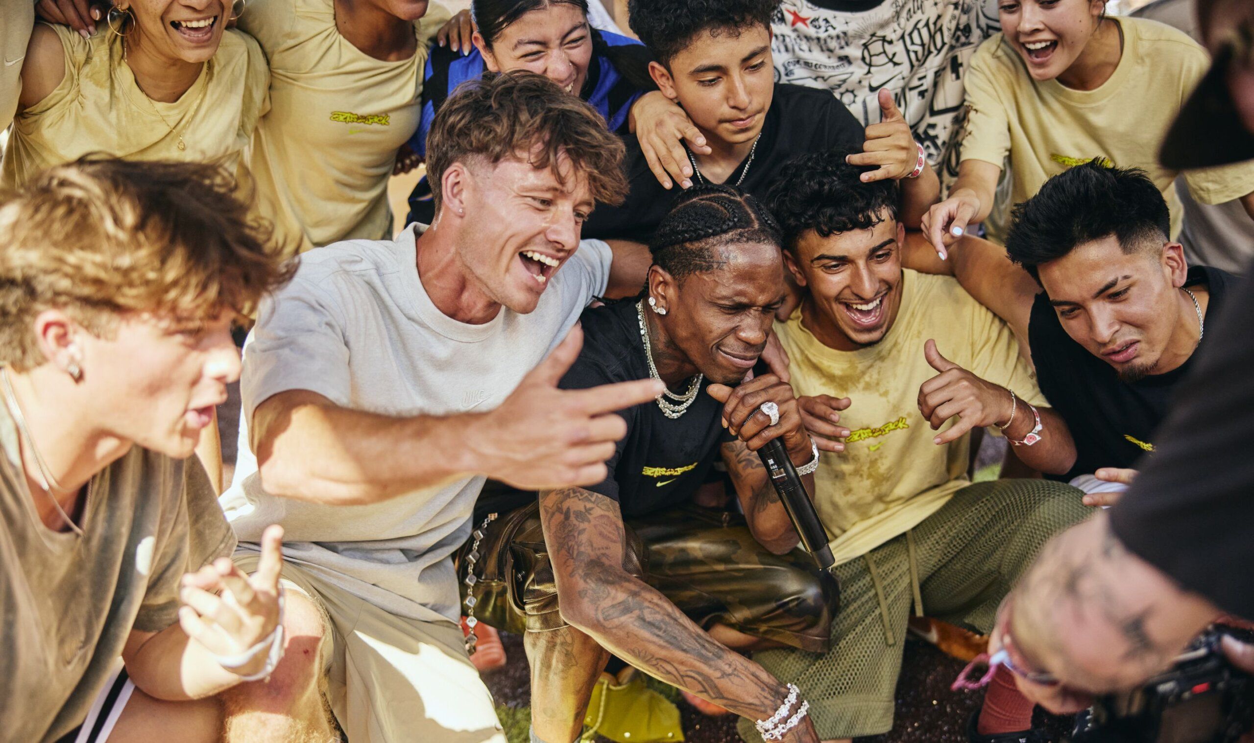 A group of young people gather closely, smiling and posing for a photo while one person in the center holds a microphone.