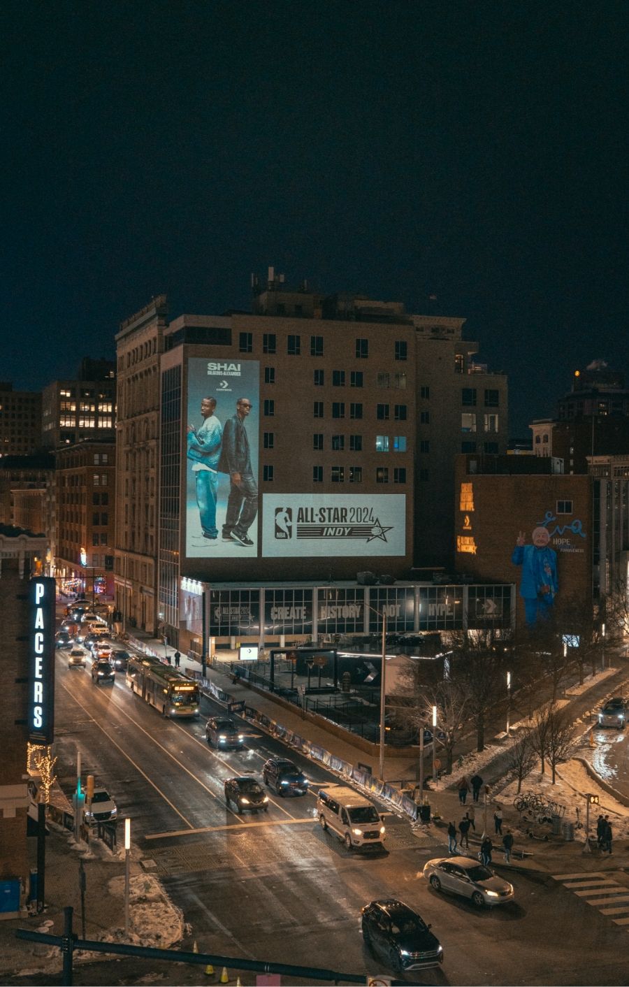 Wide shot of Converse All Star Weekend building with billboards of Shai and All Star weekend 2024. It is night time with streetlights and cars.